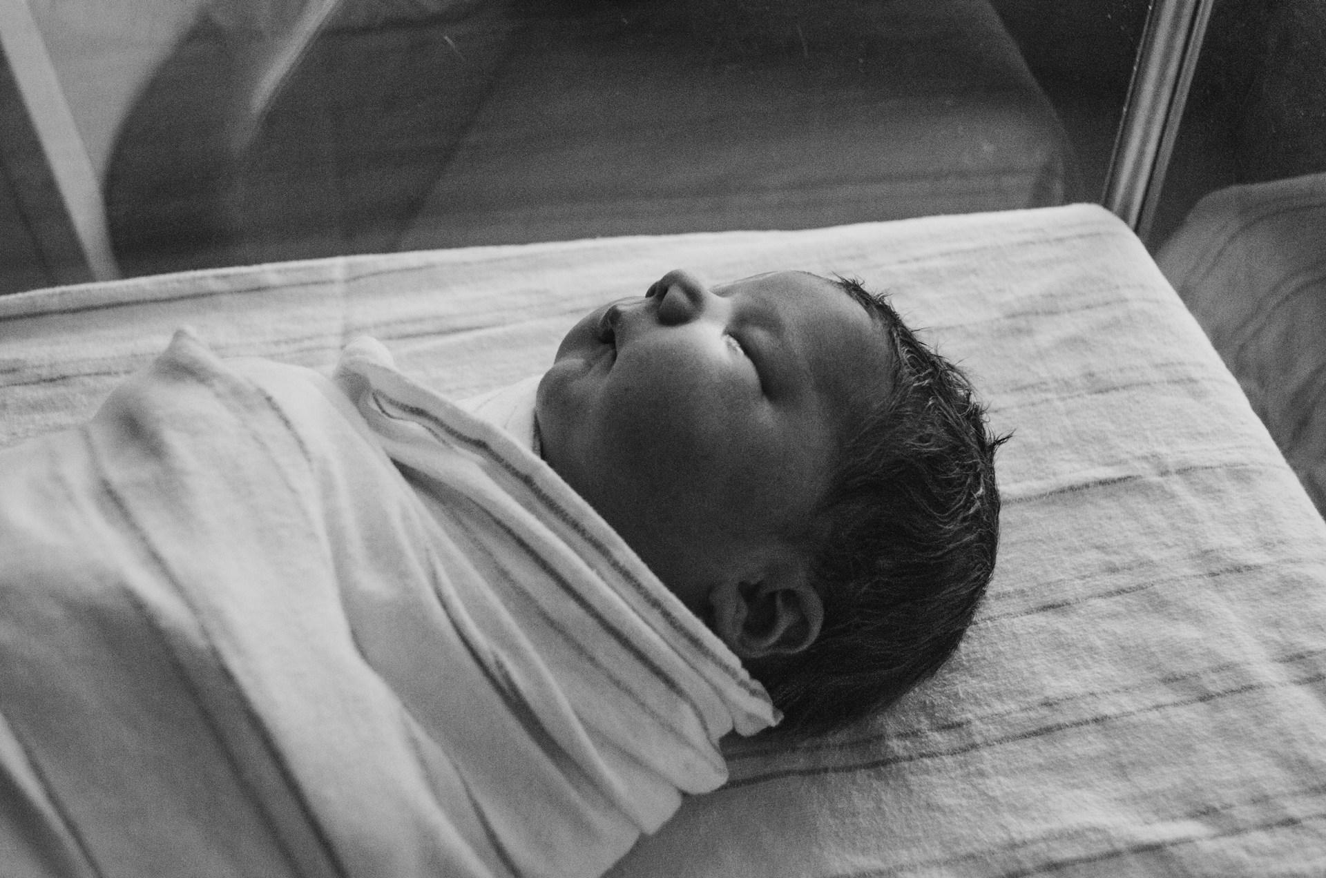 Parent wrapping newborn in a breathable muslin swaddle blanket