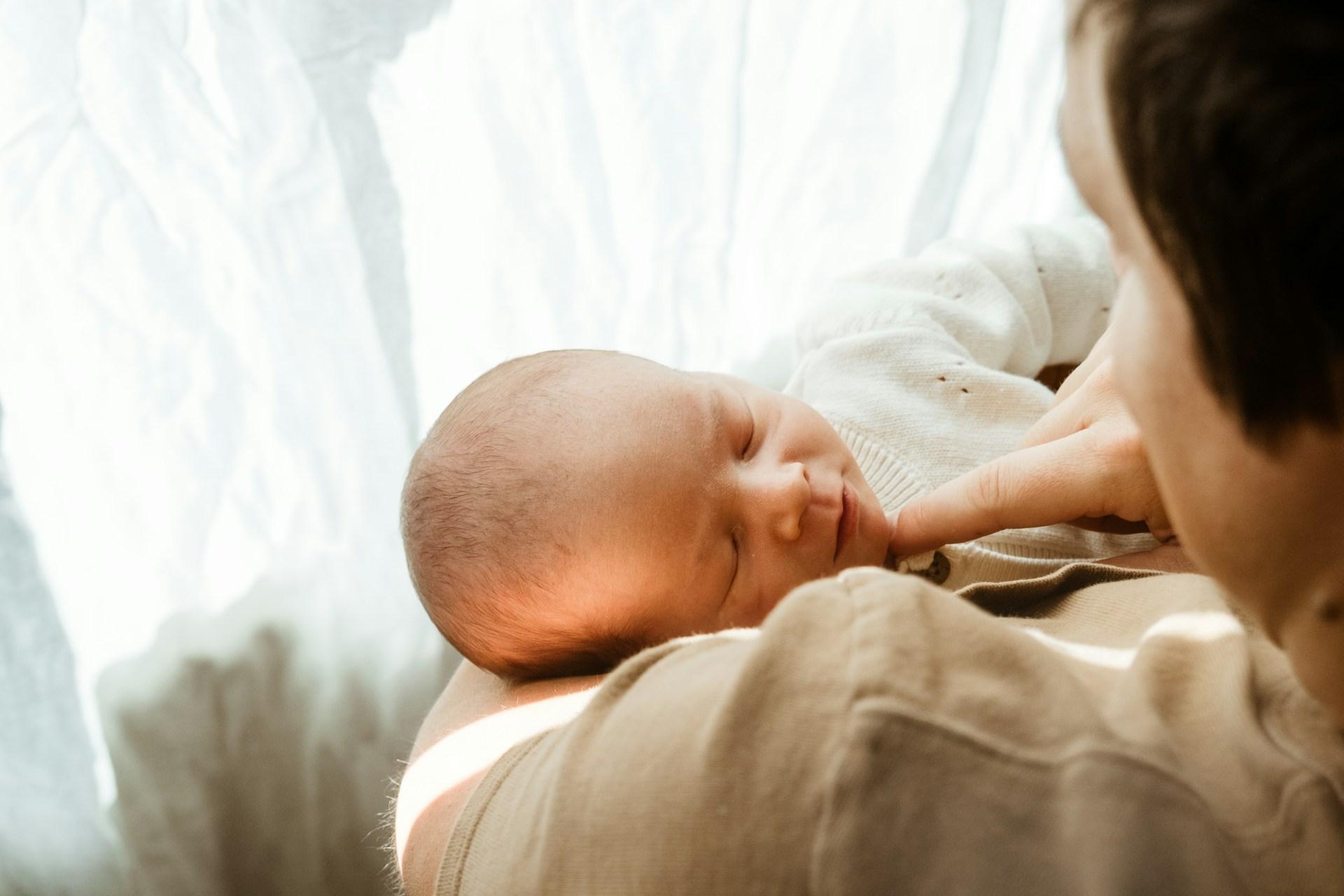 Mother breastfeeding newborn in the evening, holding baby close